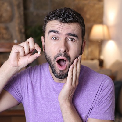 A shocked young man holding one of his missing teeth