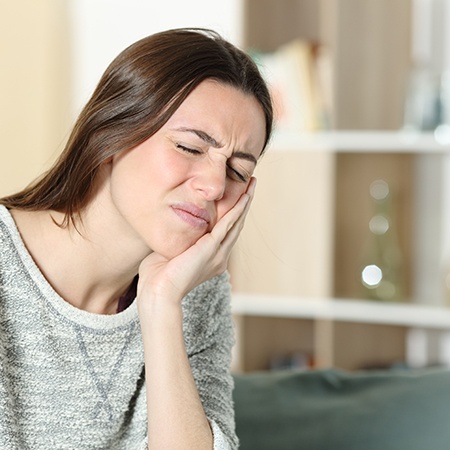 Woman in grey shirt rubbing her jaw in pain