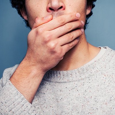 Man in need of emergency dentistry covering mouth