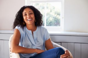 a person smiling and sitting in a chair in front of a window