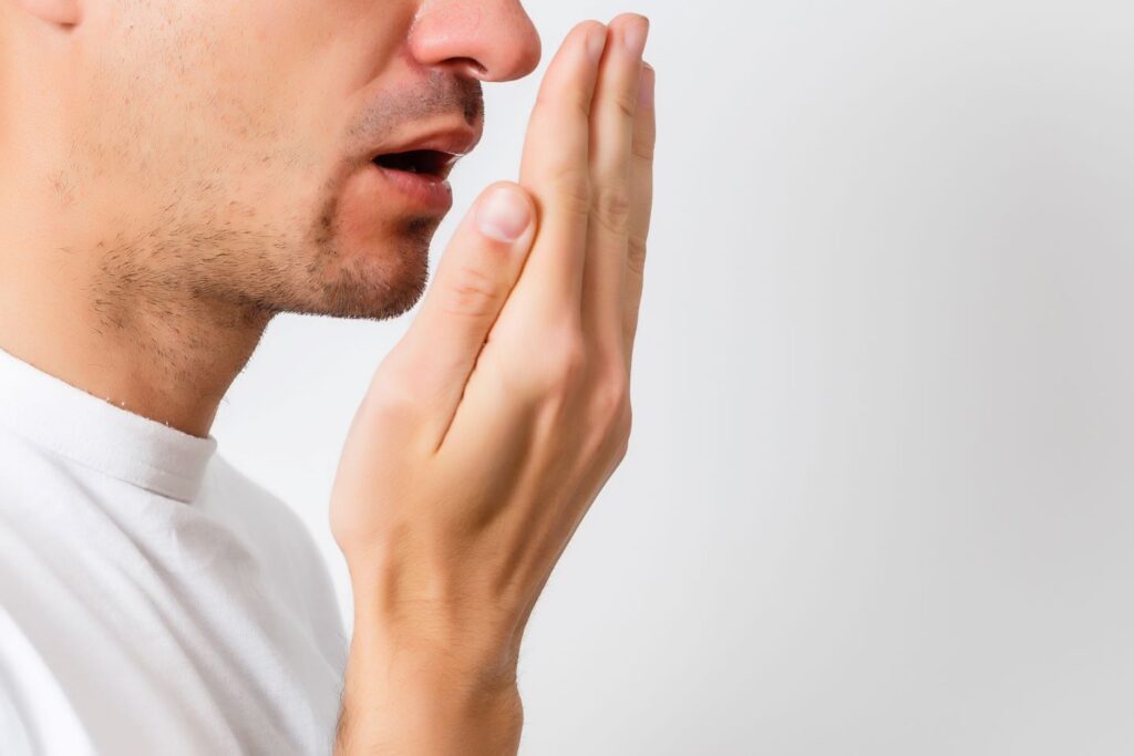 Profile view of man holding hand in front of mouth to smell breath