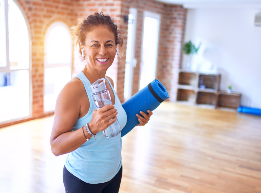Woman holding water bottle and yoga mat in fitness studio